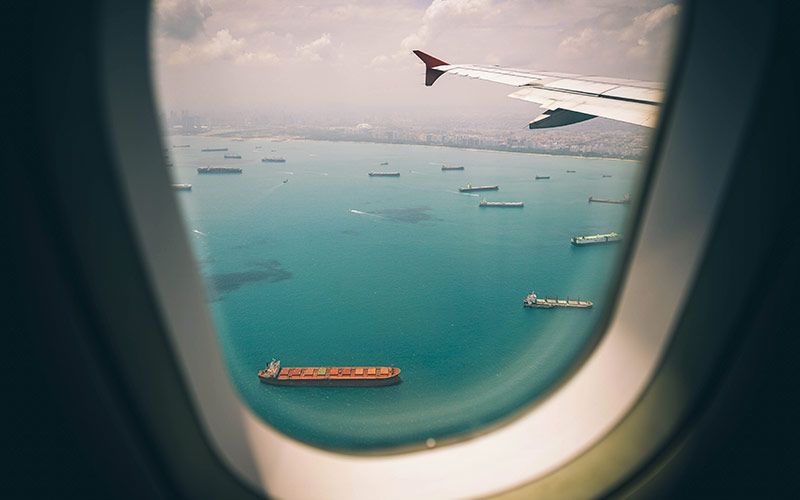 Distribución internacional y comercio exterior. Imagen de una ventana de avión viendo barcos comerciales.